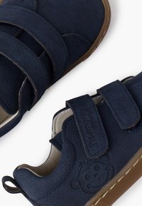 Pantofi pentru copii de culoare bleumarin, cu două benzi Velcro, partea superioară din material sintetic texturat și talpă din cauciuc. Prezintă logo-ul embosat al unui urs pe lateral.