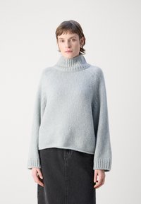 Světle šedý pletený svetr s vysokým, žebrovaným rolákem a spadlými rameny, v kombinaci s černou džínovou sukní.