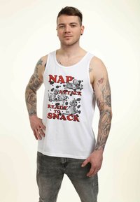 Camiseta sin mangas blanca con un estampado gráfico que presenta el texto "ATAQUE DE SIESTA, LISTO PARA PICAR" y ilustraciones de perros, combinada con unos jeans desgastados grises.