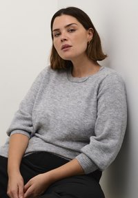 Gray knit sweater with a round neckline, short sleeves, and a ribbed hem. Soft texture and a relaxed fit. Black pants visible below.