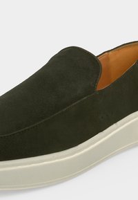Chaussure à enfiler en daim vert foncé avec une doublure intérieure beige clair et une semelle épaisse en caoutchouc blanc.