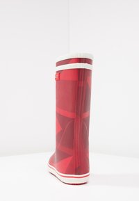 Botte de pluie en caoutchouc rouge avec une finition mate, présentant un motif géométrique et des accents blancs en haut et sur la semelle, avec une surface texturée.