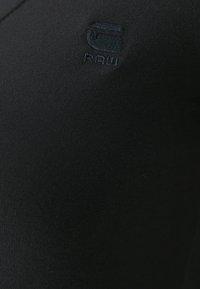 Čierna priliehavá košeľa s rebrovanou textúrou a tónovým logom s nápisom "G-RAW" vyšitým na hrudi. Hladká látka, minimalistický dizajn.
