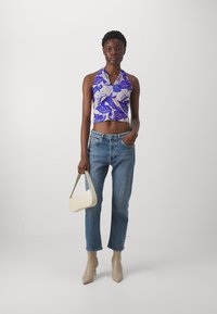 Lilla cropphette med halterneck og bladmønster, lyseblå denim jeans, nude ankelboots med hæl, og en hvid håndtaske med et enkelt håndtak.