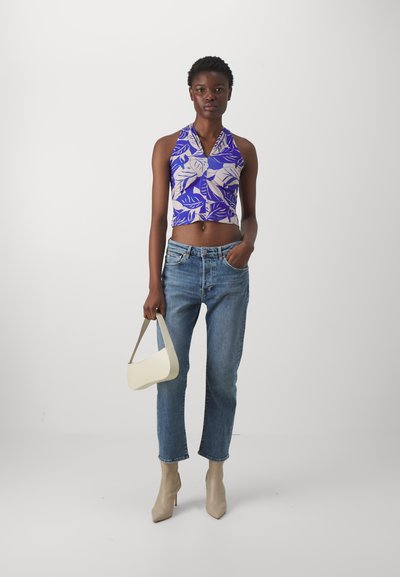 Top halter court violet avec motif de feuilles, jean en denim bleu clair, bottines à talons nudes, et un sac à main blanc à une seule anse.