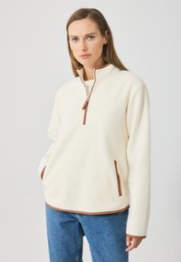 Pulover crem din fleece cu guler înalt, închidere cu fermoar pe jumătate și accente maro pe fermoar și buzunare. Textură moale și croială lejeră.