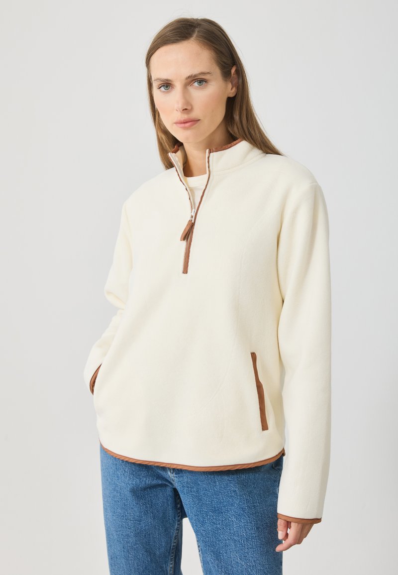 Pulover crem din fleece cu guler înalt, închidere cu fermoar pe jumătate și accente maro pe fermoar și buzunare. Textură moale și croială lejeră.