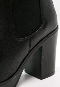 Stivaletto nero con tomaia in similpelle texturizzata, pannelli laterali elasticizzati e tacco spesso texturizzato.