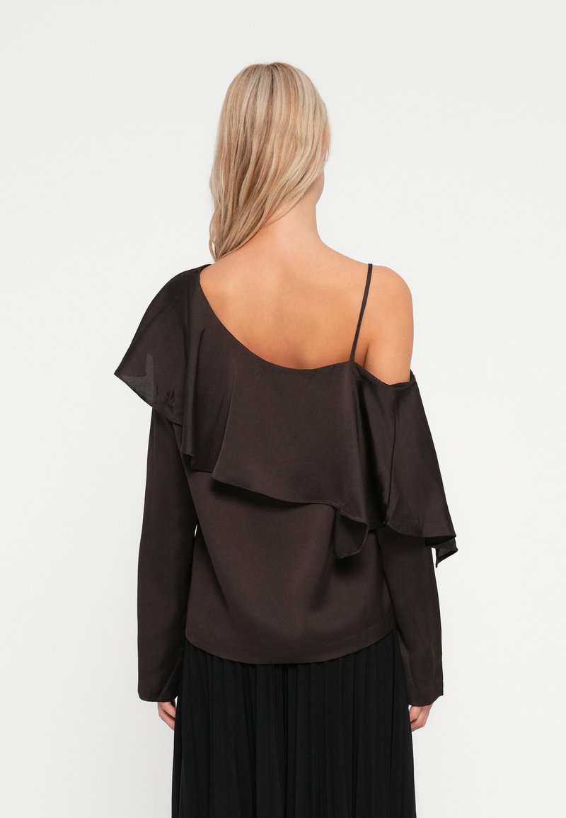 Top marron à épaules dénudées avec un design de volants superposés, manches longues et bretelles ajustables, associé à une jupe plissée noire.