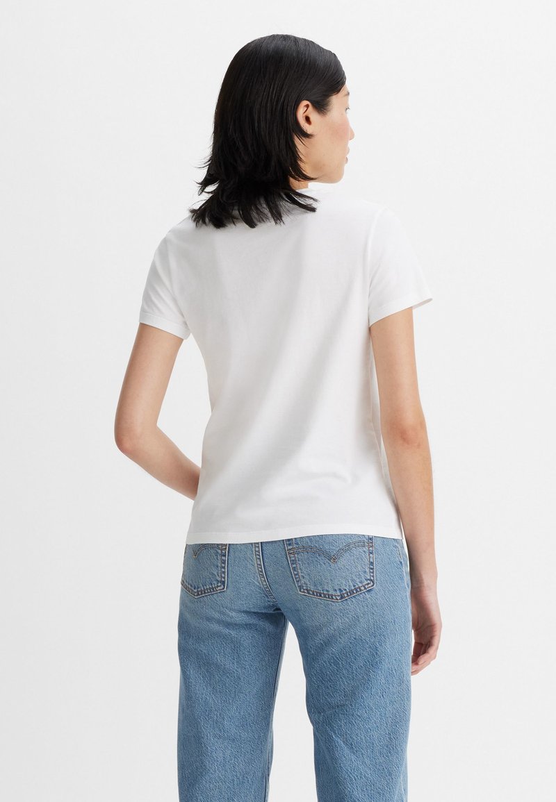 Camiseta de algodón blanca con mangas cortas, cuello redondo y un corte holgado, combinada con jeans de mezclilla azul claro que cuentan con bolsillos traseros.