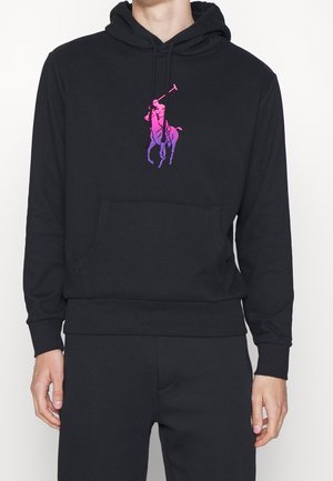 Uomo che indossa una felpa nera con tasca frontale e logo Polo Player sfumato in viola-rosa al centro del petto.