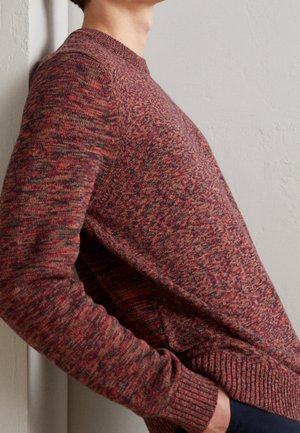 Rundhalsausschnitt Pullover in einem melierten Strickmuster mit Rottönen und Grautönen. Die gerippten Bündchen und der Saum sorgen für Struktur in der Passform.