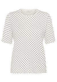 T-shirt blanc à manches courtes avec un col rond, présentant un motif de petits points noirs sur l'ensemble. Tissu doux avec une coupe décontractée.