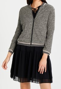 Svart och grå texturerad bomberjacka med främre dragkedja, ribbad mudd och nederkant, med randiga detaljer och en avslappnad passform.