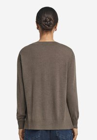 Brązowy sweter z dzianiny, z okrągłym dekoltem, długimi rękawami i prążkowanymi mankietami, o luźnym kroju i miękkiej teksturze.