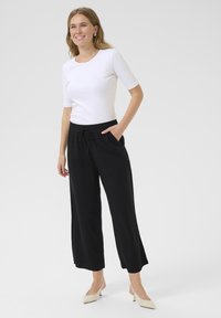 Un pantalon noir à jambes larges avec une taille élastique et un cordon de serrage, associé à un haut blanc à manches courtes. Le textile est lisse et uni.
