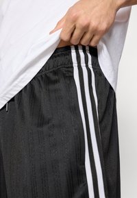 Čierne atletické šortky s textúrovaným dizajnom, bielymi pruhmi pozdĺž bočných švov a elastickým pásom.