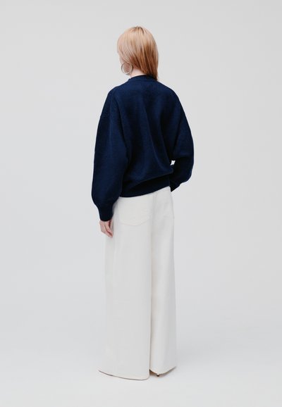 Marineblauwe trui met een relaxte pasvorm, ribgebreide manchetten en onderrand, gecombineerd met witte wijde broek, minimalistisch ontwerp, zachte textuur.