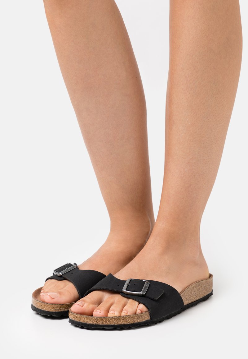 Black slide sandals with a wide strap and adjustable metal buckle, featuring a cork midsole and textured rubber outsole.