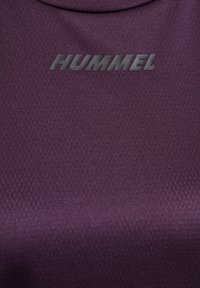Gros plan d’un tissu texturé violet foncé avec le logo « HUMMEL » en lettres noires en relief au centre.