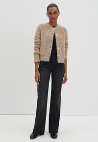Beige fuzzy cardigan with round neckline, five large buttons, and ribbed cuffs, paired with black flared jeans and black shoes.