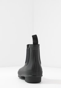 Črne gumijaste gležnjarje z elastiko na straneh, teksturiranimi navpičnimi rebrinami in z zanko na hrbtni strani za enostavno obuvanje. Ravna podplata.