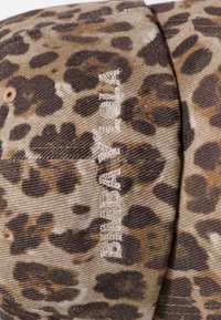 Luipaardprintstof met beige geborduurde "BILLABONG" tekst op een gestikt naaisegment.