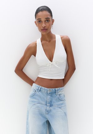 Top bianco corto con scollatura a V profonda e dettaglio annodato, abbinato a jeans a vita alta blu chiaro con sopracciglia curve.