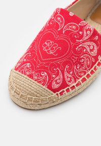 Espadrille en toile rouge avec une semelle en jute tressée beige, décorée de motifs cachemire blancs et d'un contour de cœur contenant des initiales en cursive.