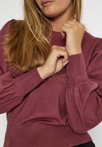 Jersey burdeos con puños y dobladillo acanalados, que presenta mangas abullonadas y un escote redondeado. Tejido suave y texturizado.