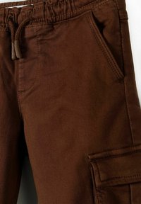 Pantalones marrones hechos de tela texturizada, con cinturilla elástica, cordón ajustable y un bolsillo lateral con solapa.