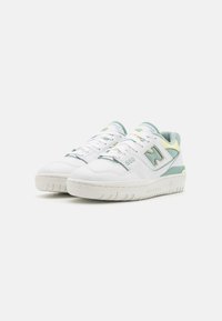 Zapatillas deportivas blancas con acentos en verde menta y amarillo pálido, detalles perforados y una suela texturizada. Presentan cordones y una marca.