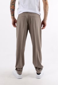 Pantaloni marroni chiari con una vestibilità dritta, texture liscia e tasche anteriori e posteriori. Abbinati a sneakers bianche.