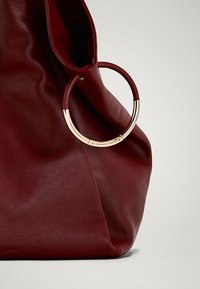 Sac en cuir cramoisi avec une forme décontractée, dotée d'une anse circulaire en métal doré et d'une texture lisse. Design minimaliste sans quincaillerie visible.