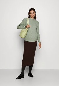 Svetlo zelena rebrasta jopica z okroglim izrezom, kombinirana s temno rjavo rebrasto midi krilo. Model drži teksturirano, pastelno zeleno torbico.