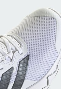 Valkoiset urheilujalkineet, joissa on hengittävä verkkomateriaali, kuvioidut mustat yksityiskohdat ja perinteinen nauhakiinnitys. Huomionarvoinen kumipohja.