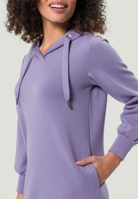 Sweat à capuche violet en tissu doux. Comprend un col en V, une capuche à cordon avec texture tressée et des poignets élastiques. Comprend des poches latérales.
