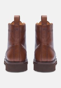 Stivali ankle in pelle marrone con finitura testurizzata, linguette posteriori e accenti perforati. Suola spessa con delicato motivo a tassello.