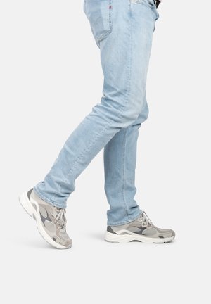 Zapatillas de deporte grises y blancas con detalles de malla y suelas de goma, combinadas con unos jeans de mezclilla azul claro. Las zapatillas presentan un diseño curvado.