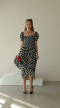 Abito a pois bianco e nero con scollatura quadrata, maniche a sbuffo e dettaglio di rosa in tessuto rosso, abbinato a tacchi alti neri.