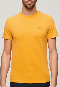 Kortærmet gul t-shirt lavet af blødt stof, med et diskret logo broderet på brystet og en klassisk rund halsudskæring.
