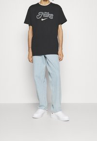 Svart bomull t-shirt med en vit och grå "Nike"-logotyp, i kombination med ljusblå denimbyxor och vita sneakers. Enkelt design, avslappnad passform.