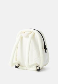Mochila blanca acolchada con material texturizado, forma curva, correas ajustables y un zipper negro. Presenta un asa de bucle para llevar.