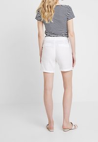 Pantaloni corti bianchi in cotone con orlo arrotolato, abbinati a una maglietta a righe bianco e nere. Design semplice, senza motivi visibili o elementi hardware.