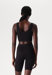 Black activewear set featuring a seamless tank top and high-waisted shorts. Textured fabric with subtle pattern, form-fitting design.