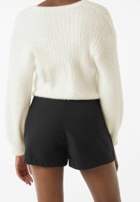 Vit, fluffig kort sweater med ribbad textur som är kombinerad med slanka, skräddarsydda svarta shorts. Outfitten har en ren, minimalistisk design.