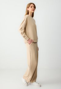 Beige sweatshirt en bijpassende broek van zacht materiaal. De sweatshirt heeft een ronde halslijn en lange mouwen; de broek heeft zijzakken en een relaxte pasvorm.