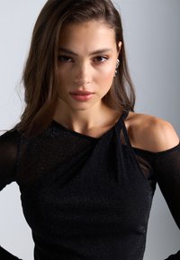 Svart topp med glans, med off-shoulder design og vridd detalj. Laget av et strukturert stoff med subtile glitringer.