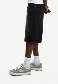 Gonna di jeans nera con taglio dritto, abbinata a sneakers grigie e bianche. Presenta tasche laterali e finiture in argento.