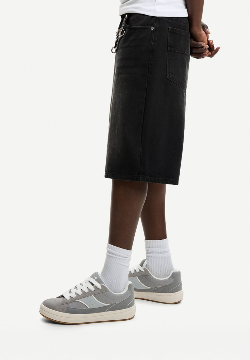 Gonna di jeans nera con taglio dritto, abbinata a sneakers grigie e bianche. Presenta tasche laterali e finiture in argento.